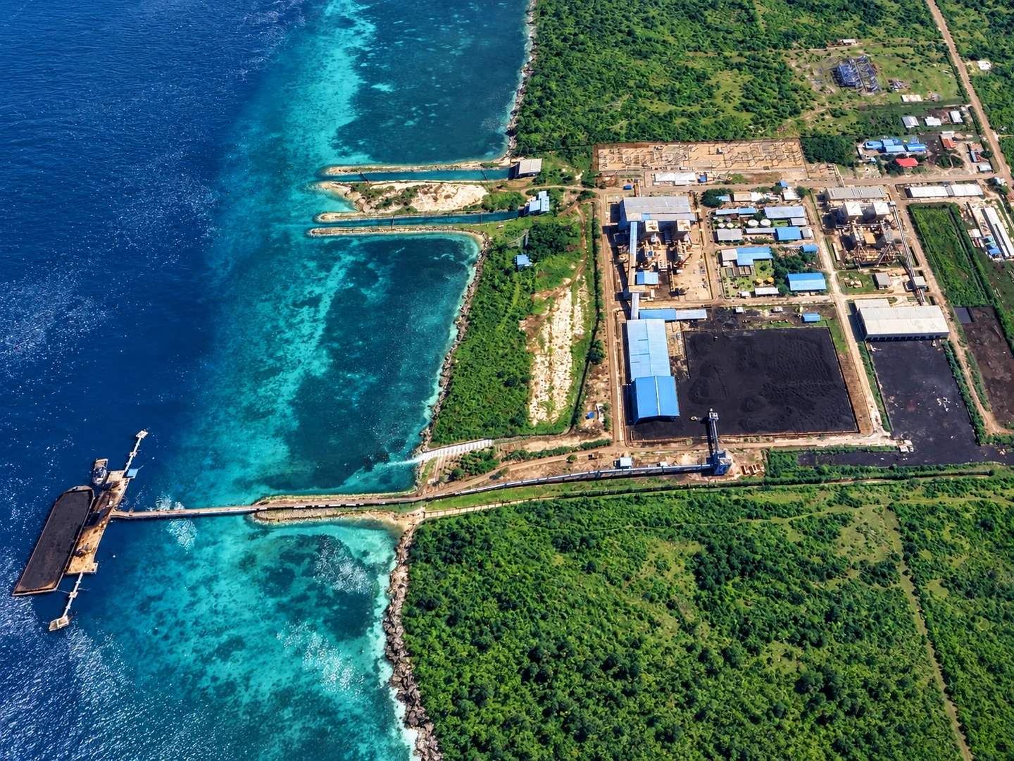 Kompleks industri di tepi laut, atap biru, jetty dan tongkang.